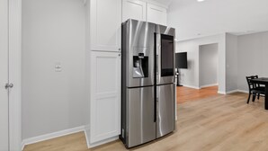 Een moderne keuken met witte kasten, een roestvrijstalen koelkast, een ingebouwd waterdispenser en een flatscreen televisie aan de muur.