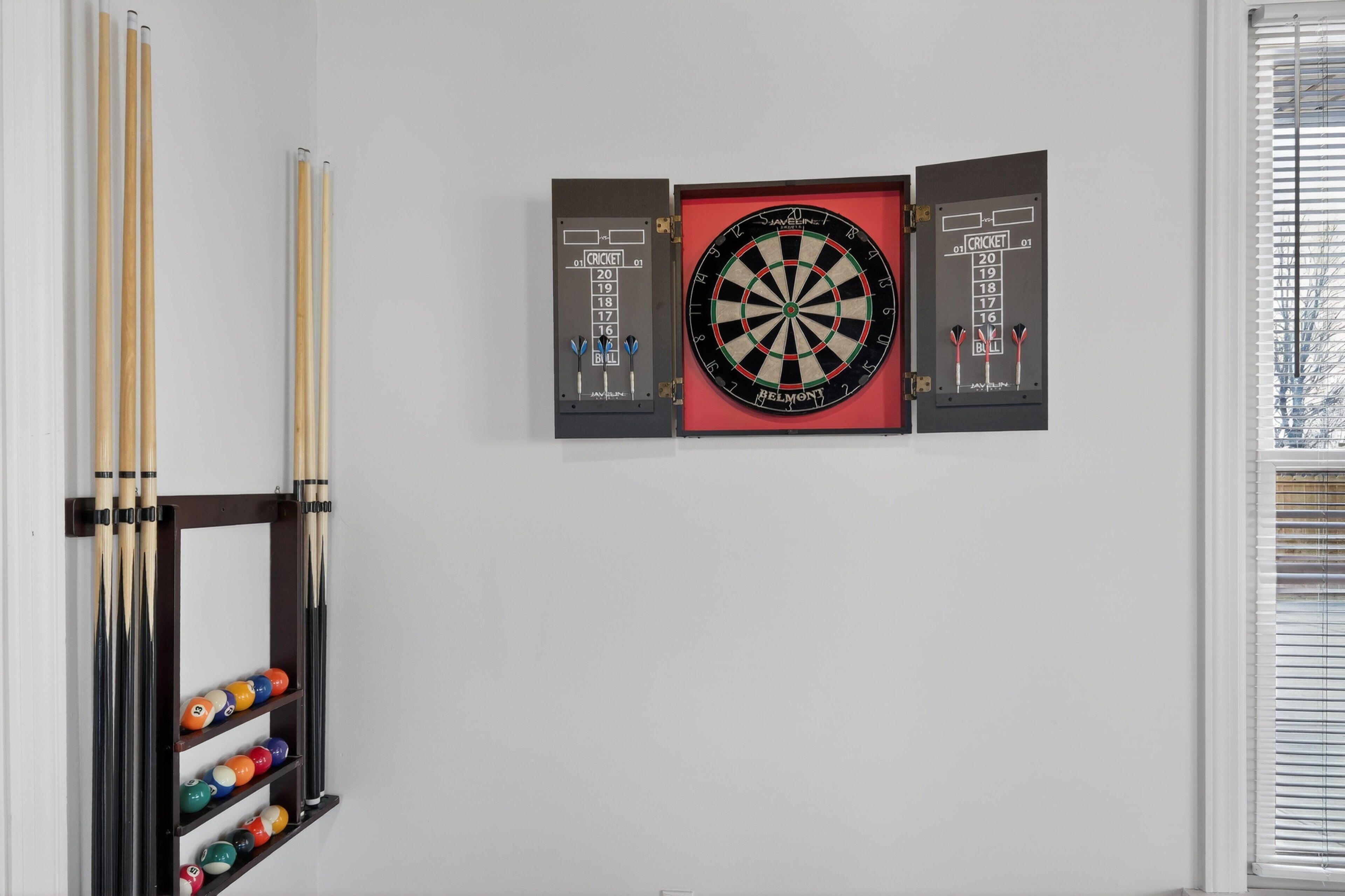 A dartboard mounted on a wall with a rack of pool cues and billiard balls below it.
