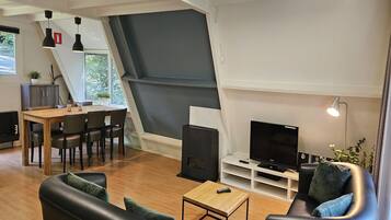 A modern living room with a wooden dining table, black leather sofa, and a flat-screen TV on a white stand.