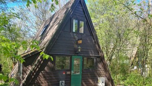 A small, dark wooden cabin with a green door, a window, and a trash can in front. - Chic Family Hideaway in Durbuy (Durbuy)