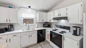 A compact kitchen with white cabinets, a microwave, a stove, a dishwasher, and a coffee maker. - Manassas Comfort Cozy 3br Family Home 3 Bedroom Home (Manassas)