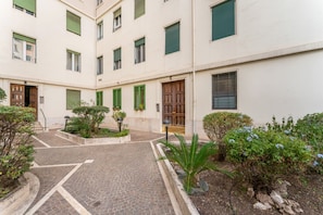 A courtyard with a paved walkway, green plants, and a building with multiple windows and doors. - La Margherita, Comfort Few Steps from San Giovanni (Roma)