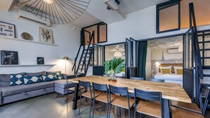 A modern living room with a wooden dining table, black chairs, a grey sofa, and a staircase leading to another room. - AN IDEAL BLEND OF COMFORT, PARISIAN CHARM-JUST STEPS FROM PLACE DE LA RÉPUBLIQUE (Paris)