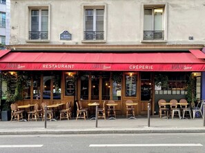 A restaurant with a red awning, outdoor seating, and a sign indicating it offers creperies. - AN IDEAL BLEND OF COMFORT, PARISIAN CHARM-JUST STEPS FROM PLACE DE LA RÉPUBLIQUE (Paris)