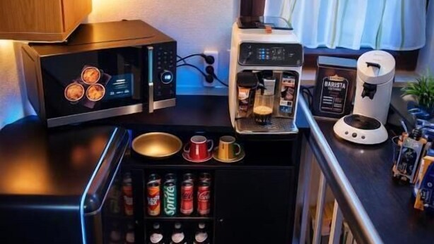 A compact kitchen with a microwave, coffee maker, and a small refrigerator. There are canned beverages and a coffee pot on the counter. - Corner Haus RM1 (Schnaittach)
