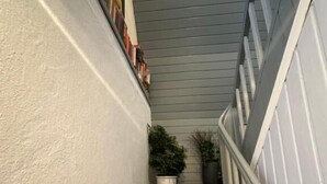 A staircase with white walls and a gray ceiling, leading to a landing area with a white railing and a potted plant. - Corner Haus RM1 (Schnaittach)