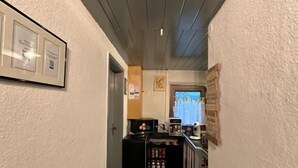 A narrow hallway with a kitchenette area at the end, featuring a microwave, coffee maker, and cabinets. - Corner Haus RM1 (Schnaittach)