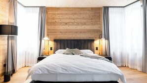 Un dormitorio moderno con techo de madera, una cama grande con ropa de cama blanca, dos lámparas de noche y cortinas de gasa.
