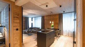 A modern living space with a wooden interior, a central kitchen island, a sofa, and a dining area. - 2-bedroom apartment in serene Andermatt perfect for your getaway, with pool (Andermatt)