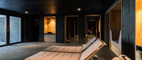 A modern spa room with two sun loungers, a stone fireplace, and large windows.