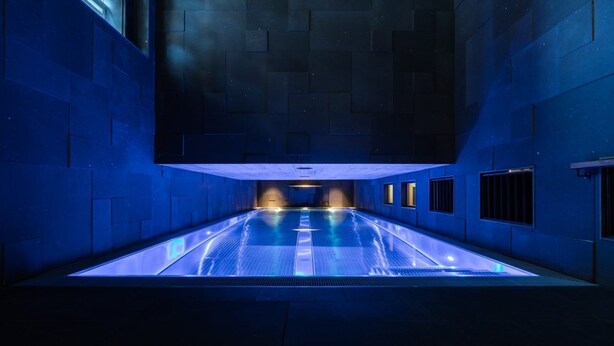 A long, narrow swimming pool with blue lighting, surrounded by walls with a geometric pattern. - 2-bedroom apartment in serene Andermatt perfect for your getaway, with pool (Andermatt)