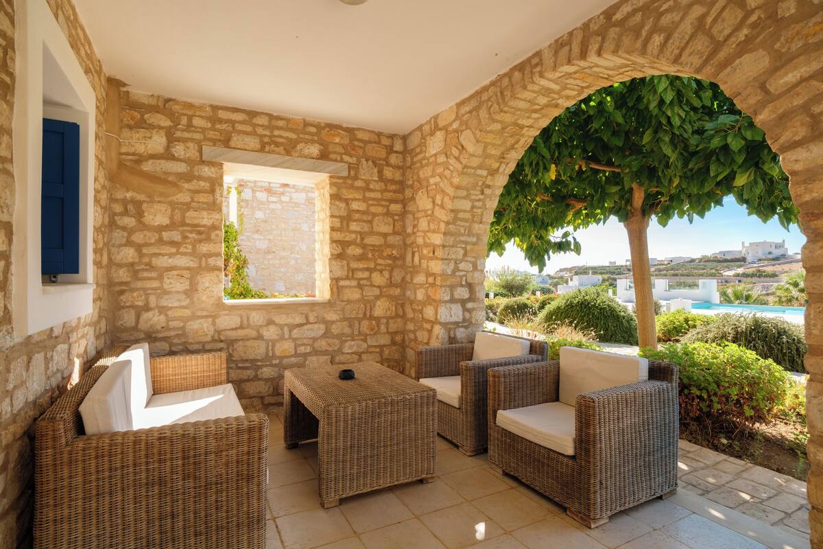 Un área de estar al aire libre con paredes de piedra, muebles de mimbre y vistas a una piscina y al paisaje.