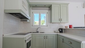 A kitchen with a window, a stove, a sink, and cabinets. - Kriolithos Houses (Paros)