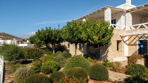 Une maison en pierre dotée d’un porche abrité, entourée de jardins bien entretenus et d’une variété d’arbustes.