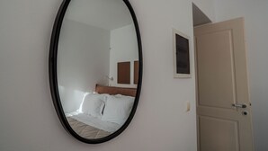A room with a bed, a door, and a wall-mounted mirror. - Kriolithos Houses (Paros)