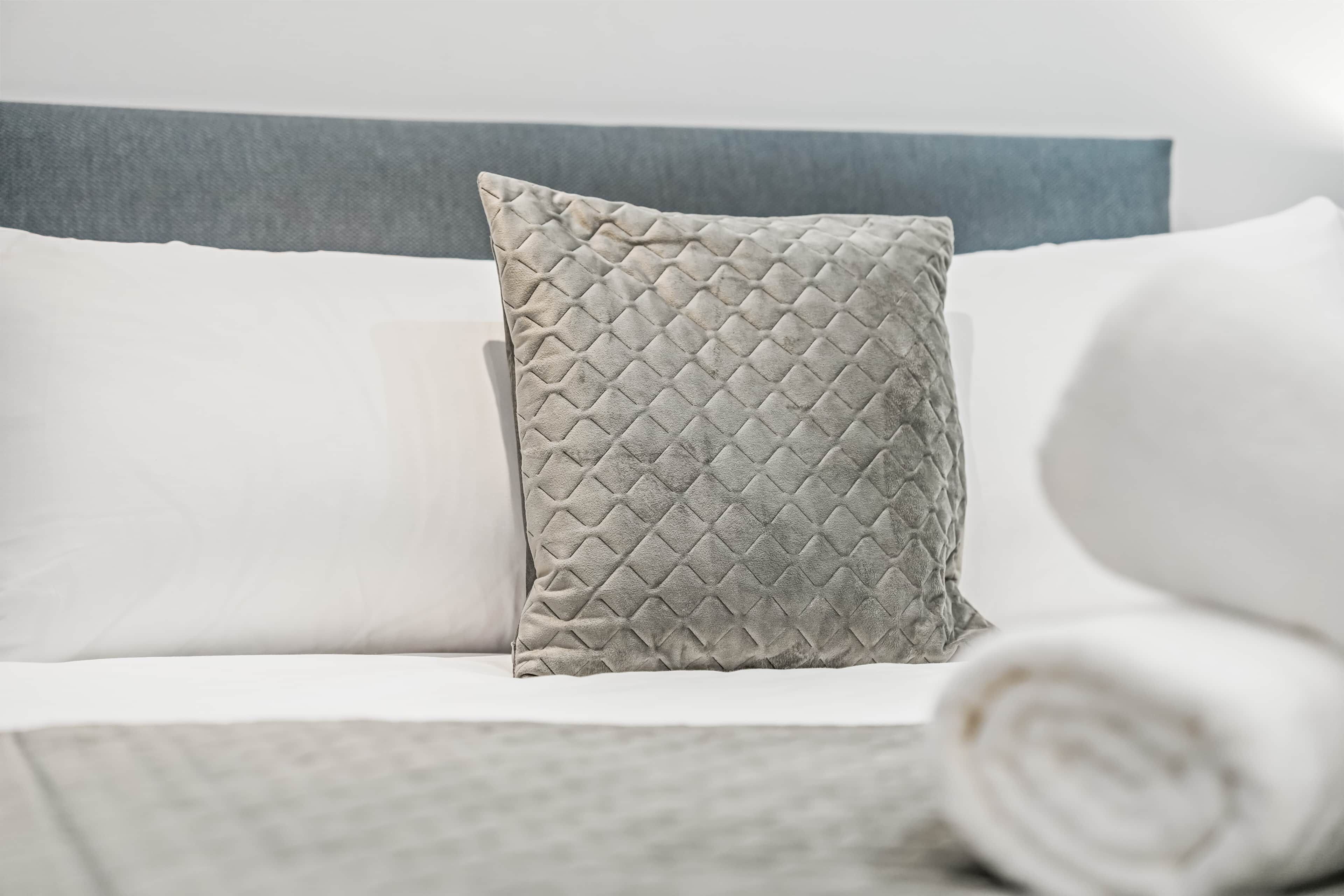 A bed with a neatly folded white blanket and a textured pillow.