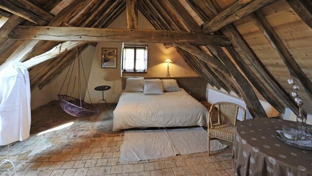 Ein gemütliches Schlafzimmer im Dachgeschoss mit Bett, Sessel und Tisch.