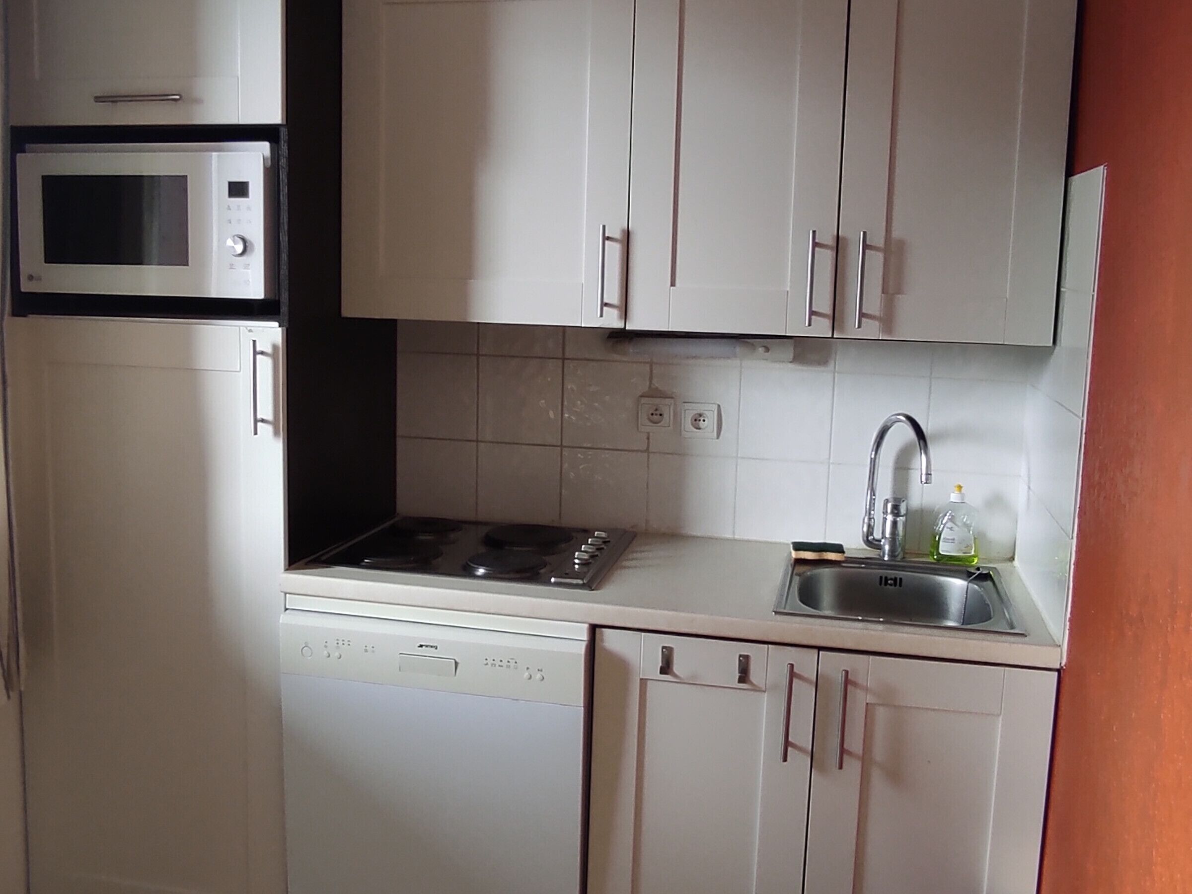 A compact kitchen with a microwave, stove, dishwasher, and a sink with a faucet.