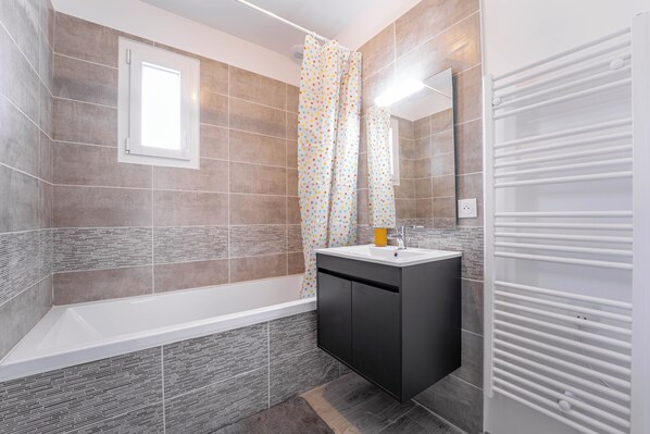 A modern bathroom with a bathtub, a vanity with a sink, and a shower curtain. - Comfortable house between forest and ocean (Mimizan)