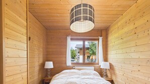 A wooden room with a bed, two bedside lamps, a window, and a plaid lamp shade. - Les Gets - 2-Bedroom Apartment Near Slopes with Balcony and Parking (Les Gets)