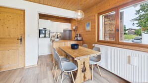A wooden interior with a dining table, chairs, a kitchen area, and a large window. - Les Gets - 2-Bedroom Apartment Near Slopes with Balcony and Parking (Les Gets)