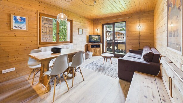 A wooden interior with a dining area, sofa, TV, and large windows. - Les Gets - 2-Bedroom Apartment Near Slopes with Balcony and Parking (Les Gets)
