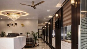 Un hall d’hôtel comprenant un comptoir d’accueil, un lustre, des ventilateurs de plafond et un long couloir avec des lambris en bois et des portes en verre.