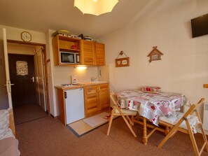 A compact kitchen with wooden cabinets, a microwave, and a small refrigerator. There is a dining table with a tablecloth and chairs. - Cozy studio for 3, piste view (Morillon Village)