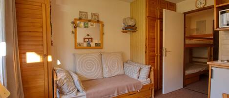 Una habitación acogedora con un sofá de madera, una mesita, una cama litera y un espejo en la pared.