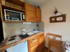 A compact kitchen with wooden cabinets, a microwave, a coffee maker, and a sink. - Cozy studio for 3, piste view (Morillon Village)