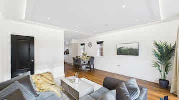 A modern living room with a grey sofa set, a coffee table, and a dining area in the background.