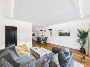 A modern living room with a grey sofa set, a coffee table, and a dining area in the background. - Luxurious 4-Bedroom Home | Sleeps 12 Guests | High-Speed WiFi | Free Parking (South Croydon)
