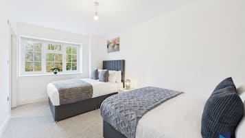 A bedroom with two beds, a window with a view of trees, a bedside table with a lamp, and a painting on the wall.
