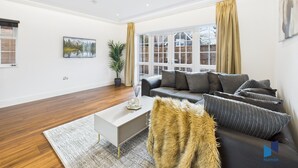 A modern living room with a sofa, coffee table, and a large window with curtains. - Luxurious 4-Bedroom Home | Sleeps 12 Guests | High-Speed WiFi | Free Parking (South Croydon)