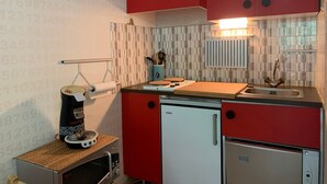 A compact kitchen with red cabinets, a small refrigerator, a coffee machine, and a tiled backsplash. - Bright studio 4 pers, balcony, close to slopes Pra-Loup 1600 (Pra-Loup)