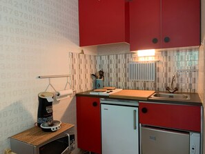 Eine kleine Küche mit roten Schränken, einem kleinen Kühlschrank, einer Kaffeemaschine und einer gefliesten Spritzschutzwand.