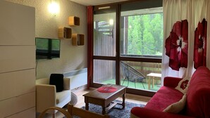 A cozy living room with a sofa, a small table, a TV mounted on the wall, and a window with curtains. - Bright studio 4 pers, balcony, close to slopes Pra-Loup 1600 (Pra-Loup)