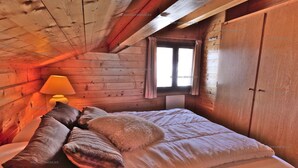 Ein gemütliches Holzblockhaus-Zimmer mit Bett, Kissen, einer Lampe und einem Fenster.