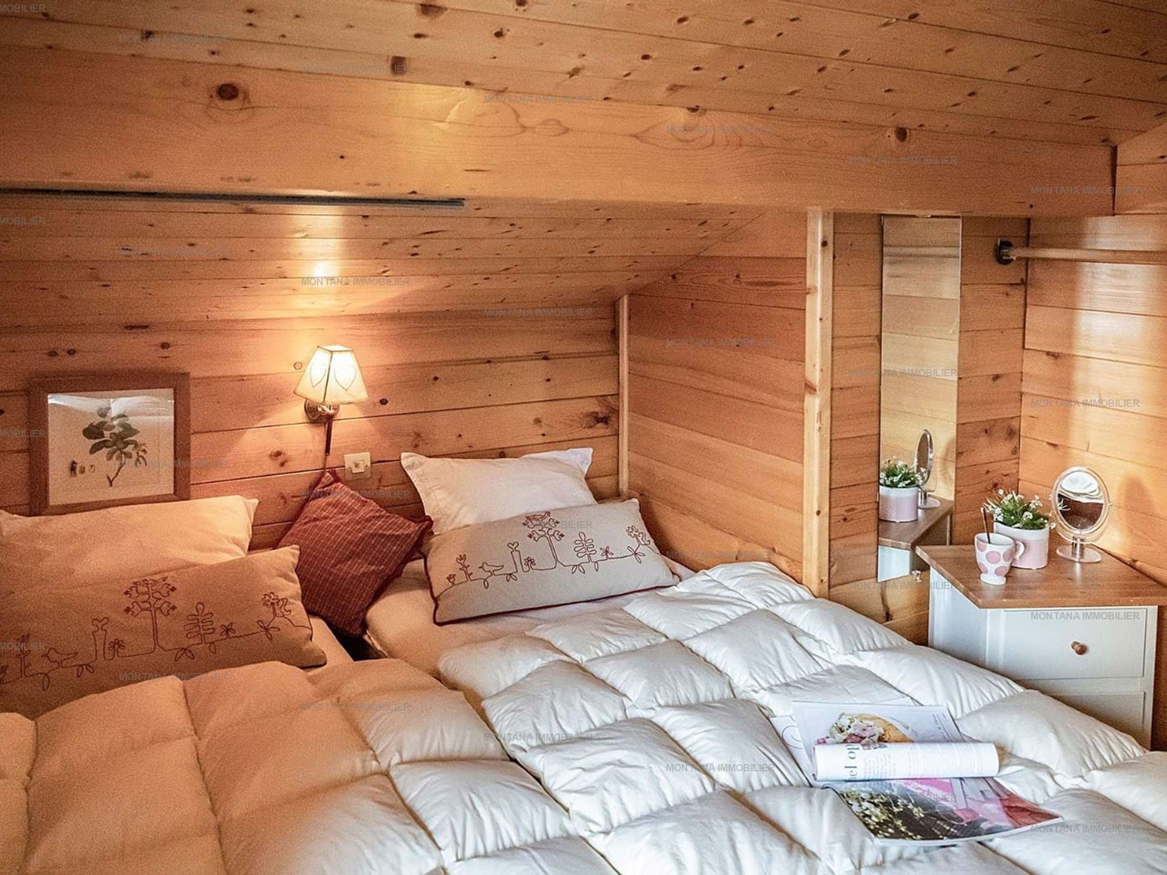 Une chambre confortable avec un plafond en bois, un lit avec une literie blanche, une table de chevet avec une lampe et une petite commode avec un miroir.