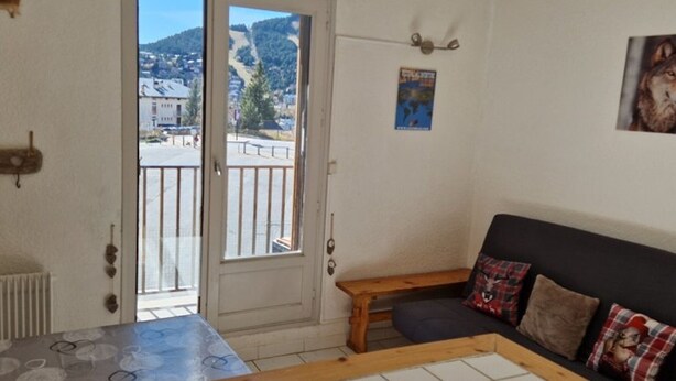 Ein Zimmer mit Blick auf eine Stadt durch eine Schiebetür, ein kleiner Holztisch, eine Couch mit Karokissen und ein Poster an der Wand.