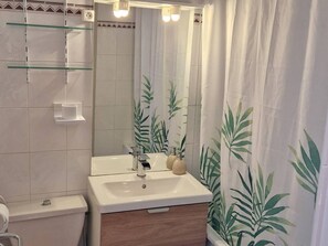 Ein Badezimmer mit einem weißen Waschbecken, einem Spiegel und einer Duschvorhang mit Blätermotiv.