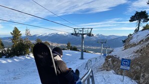 Sessellift mit einer Person, verschneite Landschaft und Bergen im Hintergrund.