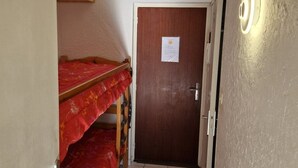 Ein schmaler Flur mit einem Holzbett, einer Tür mit einem Hinweis und einer Wandleuchte.