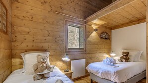 Una habitación de cabaña acogedora con dos camas, paredes de madera, un ventanal y un osito de peluche sobre una de las camas.
