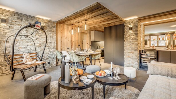 Una sala de estar moderna con pared de piedra, techo de madera y comedor con mesa y sillas de madera.