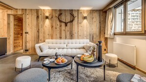 Una sala de estar moderna con un muro de madera, un sofá, dos mesitas con fruta y vino, y un radiador.