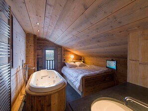 A wooden cabin bedroom with a wooden bathtub, a bed, a TV, and a view of the mountains through a window. - Apartment on the slopes with parking in Courchevel 1850 (Courchevel 1850)