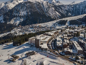 A snow-covered mountain town with a central building complex, ski slopes, and a backdrop of rugged mountains. - Apartment on the slopes with parking in Courchevel 1850 (Courchevel 1850)