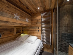 A wooden cabin room with a bed, a shower area, and wooden walls. - Apartment on the slopes with parking in Courchevel 1850 (Courchevel 1850)