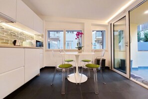 A modern kitchen with white cabinets, a round table with green chairs, and a view of the city through large windows. - CASA INDIPENDENTE A PRATI (ROMA)